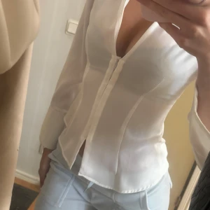 Vit v-ringad skjorta från Zara - Säljer en stilren vit skjorta från Zara i storlek XS. Skjortan har v-ringning, lång ärm och en figurnära passform. Materialet är tunt och lätt, aldrig använd endast testad 