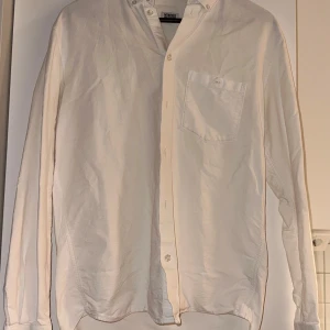 Vit långärmad skjorta från Weekday - Vit skjorta från Morris med klassisk krage och knappstängning framtill. Har en bröstficka med knapp och långa ärmar med manschettknappar. Skjortan är tillverkad i mjuk bomull och har en stilren, normal passform som funkar till många olika looks.