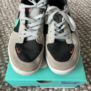 Nike SB Force 58 sneakers grå/svart - Nike SB Force 58 sneakers med grå mocka, svart tåparti och mesh i grått. Mintgrön swoosh på sidan och små röda swooshes på tån och sulan. Skorna har snörning och vit platt sula, perfekt för skate eller streetstyle. Nypris: 1500kr, säljes med originalkartong för 500kr