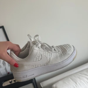 Nike Air Force 1 Flyknit vita sneakers - Säljer ett par fräscha Nike Air Force 1 Flyknit sneakers i helvitt. Skorna har klassisk låg siluett, stickad ovandel med snygg struktur och vit swoosh på sidan. Platt sula med AIR-dämpning och snörning framtill. Perfekta för dig som gillar cleana och sportiga vibes.