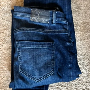 Mörkblå Kingsley jeans med raka ben - Snygga mörkblå jeans från Kingsley med klassisk femficksdesign och raka ben. Jeansen har tydliga kontrastsömmar och en stilren läderpatch bak i midjan. Materialet är slitstarkt denim som ger en cool och tidlös vibe. Perfekt för dig som gillar enkel och clean stil.