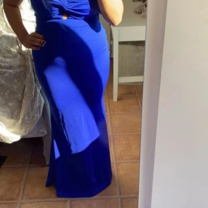 Kornblå långklänning med oneshoulder - Säljer en kornblå långklänning med snygg oneshoulder och twistad detalj vid bysten. Klänningen har en figurnära passform och en liten cut-out framtill. Perfekt för dig som vill sticka ut med en elegant och modern look.