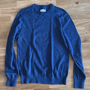 Merinoull tröja - En stilren blå stickad tröja från Marc O'Polo med rund halsringning och långa ärmar. Tröjan har en klassisk passform och ribbade muddar vid ärmslut och nederkant. Perfekt för lager-på-lager och enkel att matcha med jeans eller chinos.