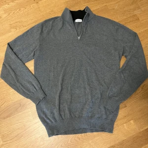 Grå half zip tröja John Henric M - Snygg grå långärmad tröja från John Henric med half zip-dragkedja och hög krage. Tröjan är i mjuk bomull och har ribbade muddar vid ärmslut och nederkant. Perfekt för lager-på-lager och chill stil.