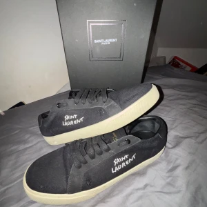 Svarta Saint Laurent sneakers strl 43 - Svarta sneakers från Saint Laurent med vit logotyp på sidan. Skorna har snörning, rund tå och platt sula i beige ton. Tillverkade i canvas och detaljer i skinn. Snygg minimalistisk design som passar till streetwear och casual outfits. Skorna är i topp skick och har äktehetsbevis. Allt som är på bilder ingår i köpet! Säljs nu jätte billigt eftersom jag eftersträvar pengar snabbt! Alltså nypris 6199 men mitt pris 2349kr!!!😀🤝Men vid riktigt snabb affär är priset ej hugget i sten🔨🪨