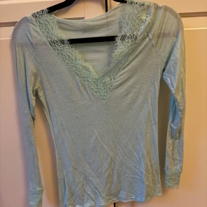Mintgrön/turkos Intimissimi topp - Supersöt mintgrön/turkos långärmad topp från Intimissimi med v-ringning och spets vid halsringning och ärmslut. Ultralätt material med cashmere för extra lyxig vibe. Använd en gång så toppskick