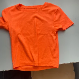Ribbad orange t-shirt - En riktigt snygg orange t-shirt med ribbad struktur och klassisk rund hals. T-shirten har korta ärmar och är gjord i ett mjukt material som känns skönt mot huden. Perfekt för dig som vill sticka ut med färg och enkel stil.