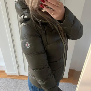 Mörkgrön Moncler dunjacka med päls - Säljer en snygg mörkgrön dunjacka från Moncler med huva och avtagbar pälsdetalj. Jackan har Moncler-logga på ärmen, dragkedja framtill och quiltad design. Perfekt för kalla dagar och har en riktigt schysst passform som sitter normal.