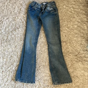 Blå bootcut jeans Gina Tricot 158 - Snygga blå jeans från Gina Tricot i storlek 158. Modellen har bootcut-ben och klassisk femficksdesign. Jeansen har en ljus tvätt och är tillverkade i jeansmaterial med dragkedja och knapp framtill. Perfekta för dig som gillar en nice vibe.