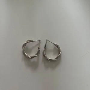 Silvriga tvinnade hoops örhängen - Säljer ett par snygga silvriga hoops med tvinnad design. De är runda och har en cool, chunky känsla som passar perfekt till din stil. Lätta att bära och stängs med klassiskt lås. Perfekta för att lyfta vilken outfit som helst.
