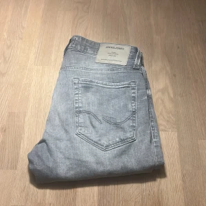 Grå slim jeans från Jack & Jones - Snygga ljusgrå jeans från Jack & Jones i modellen Slim Glenn. Jeansen har klassisk femficksdesign, normal midja och raka ben. Materialet är mjukt denim i bomull med lite stretch för extra komfort. Perfekt för dig som gillar en clean och modern look.
