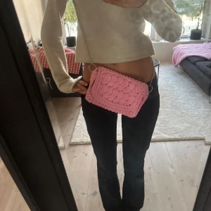 Rosa stickad axelväska med kedja - Säljer en supergullig rosa axelväska med stickad struktur och silverfärgad kedja. Väskan har en rektangulär form och är perfekt för att bära det viktigaste. Den mjuka stickade ytan ger en unik och trendig vibe som verkligen sticker ut.