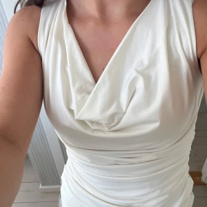Vit draperad ärmlös topp - Helt ny med lappen kvar. Säljer en vit ärmlös topp med snygg draperad halsringning och figurnära passform. Toppen har en lätt glansig yta och är stretchig, vilket gör den superbekväm och smickrande. Perfekt att styla med jeans eller kjol för en clean look. Från hm i storlek S. 