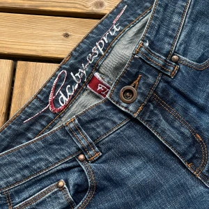 Blå Lågmidjade Jeans - Snygga blå jeans med kontrastsömmar och broderad detalj på bakfickorna. Säljer då de ej kommer till användning. 