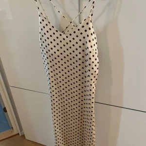 Prickig långklänning från MNG - Snygg långklänning från MNG i ljus beige med bruna prickar. Klänningen har smala axelband som korsas i ryggen och en v-ringad front. Materialet är mjukt och har en satinliknande finish som ger en lyxig känsla!🥰