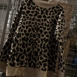 Leopardmönstrad stickad polotröja från NA-KD - Säljer en beige och svart stickad polotröja från NA-KD med leopardmönster. Tröjan har lång ärm, bred ribbad polokrage samt ribbade muddar vid ärmslut och nederkant. Perfekt för dig som gillar djurmönster och vill ha en mysig tröja. Aldrig använd bara legat i garderoben! 