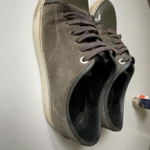 Grå mockasneakers från Lanvin - Säljer ett par grå sneakers från Lanvin med ovandel i mocka och tåparti i mörkare grått. Skorna har vita sulor och klassisk snörning. Perfekta för dig som gillar stilrena och tidlösa sneakers. Pris kan diskuteras