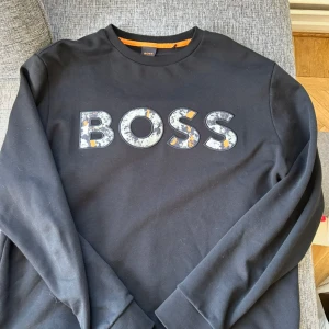 Svart sweatshirt från BOSS med tryck - Hjälper min kille att säljas hans Hugo Boss swetshirt i storlek L. Tröjan är köpt på inside för 1800 kr och är knappt använd. 