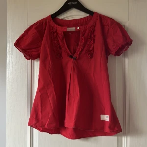 Odd Molly blus - Röd blus från Odd Molly med korta puffärmar, volangdetaljer längs ringningen och en liten rosett framtill 💞