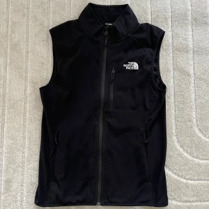 Svart väst från The North Face - Säljer en svart väst från The North Face med dragkedja framtill och hög krage. Västen har en bröstficka med dragkedja och två sidofickor. Perfekt för lager-på-lager. • Storlek M • Frakt tillkommer  • Har du några frågor är det bara att skicka ett meddelande, så svarar jag så fort jag kan.☺️ Ha en fin dag!💕♻️