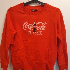 Röd Coca-Cola sweatshirt från LMTD - Cool röd sweatshirt från LMTD med Coca-Cola Classic-tryck och flaska framtill. Tröjan har rund halsringning och långa ärmar.