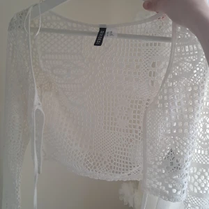 Vit spetskofta - Säljer en vit, croppad spetskofta från Divided h&m. Koftan har lång ärm och är tillverkad i ett genombrutet, virkat material som ger en luftig och trendig look. Perfekt att slänga över ett linne eller klänning för en extra touch.