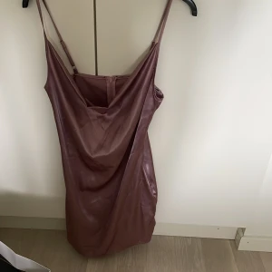 Rosa axelbandslös klänning i syntetmaterial - Säljer en snygg rosa klänning med smala axelband och draperad framsida. Klänningen har en figurnära passform och är tillverkad i ett glansigt syntetmaterial. Perfekt för dig som vill sticka ut lite extra!