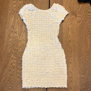 Klänning med öppen rygg - Supersöt vit kortklänning med unik strukturerad yta och korta ärmar. Klänningen har en tight passform och är perfekt för sommarens alla tillfällen. Klänningen har en djup öppen rygg! 