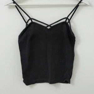Svart croppad linnetopp med dubbla axelband från Brandy Melville - Säljer en svart croppad linnetopp från Brandy Melville med dubbla smala axelband och snygg detalj vid urringningen. Perfekt till sommaren och enkel att matcha med olika outfits.