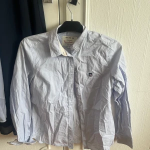 Ljusblå skjorta från Bondelid - Säljer en klassisk ljusblå skjorta från Bondelid med krage och knappar framtill. Skjortan har lång ärm och en liten broderad logga på bröstet. Perfekt för en stilren och enkel look. Inte använd någon gång. 💘