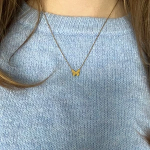 Guldigt Edblad halsband med fjärilshänge - Säljer ett fint halsband i 14K guldplätering med ett litet fjärilshänge. Kedjan är tunn och smidig, perfekt för att ge en söt detalj till din outfit. Lås med karbinhake och justerbar längd 42-45cm. Orginalpriset är 300kr. Orginallåda eller kvitto ingår inte då jag fick halsbandet i present.
