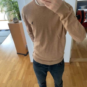 Ralph Lauren Finstickad Tröja - Säljer en stilren beige tröja från Ralph Lauren i slim fit. Tröjan är i färgen beige och storlek M men sitter stort så passar även L. Nypris ligger på 1899 och den är i väldigt bra skick. Hör gärna av er vid frågor eller funderingar!!