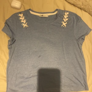 Blå t-shirt med snörningsdetaljer från FB Sister - Säljer en ljusblå t-shirt från new  yorker Sister i storlek L. T-shirten har korta ärmar och snygga vita snörningsdetaljer vid axlarna som ger en unik touch. Perfekt för dig som vill ha något enkelt men ändå speciellt. 