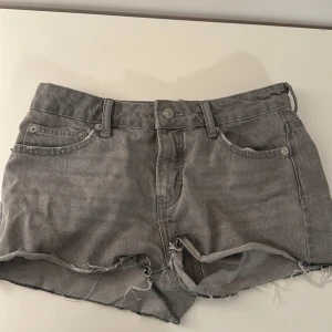 Grå jeansshorts med fransar från 157 - Gråa jeansshorts från 157 med råa fransade kanter och slitningar framtill. Klassisk femficksmodell med knappgylf och bälteshällor. Perfekta för en avslappnad stil.