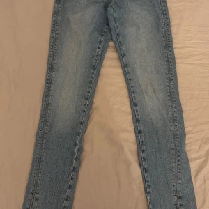 Blå jeans med slits från Zara - Säljer ett par klassiska blå jeans från Zara med raka ben och snygga slitsar nertill. Jeansen har råa kanter vid benslut och normal passform. Perfekta till en avslappnad stil och lätt att matcha med olika toppar.