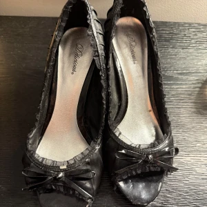 Svarta klackar med rosett och öppen tå - Skorna är aldrig använda men köpta second hand. Säljer pga att de är för stora för mig. Storleken står inte på men jag är storlek 38/39 och de är precis för stora. Skulle gissa på strl 40