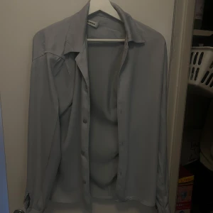 Ljusgrå skjorta från Sandro - Säljer en stilren ljusgrå skjorta från Sandro med klassisk krage och knäppning framtill. Skjortan har långa ärmar och är tillverkad i ett mjukt, slätt material som känns skönt mot huden. Perfekt för en clean och enkel look.