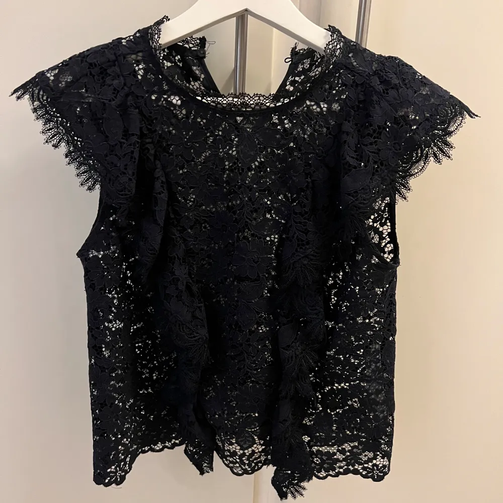 Säljer en marinblå blus i spets med vackra volangdetaljer vid axlarna. Blusen är ärmlös och har en rund halsringning. Perfekt för dig som vill ha en trendig och elegant topp till garderoben. storlek XS, från Zara. Yläosat.