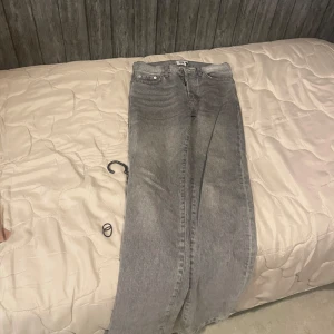 Grå jeansbyxor med rak passform - Säljer ett par grå jeansbyxor med klassisk femficksdesign och rak passform. Byxorna har normal midja och stängs med dragkedja och knapp. Perfekta till en avslappnad stil och passar till mycket. Storlek W27 L32.