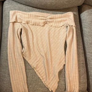 Beige ribbad offshoulder topp - Trendig beige offshoulder topp med långa ärmar och croppad, spetsig nederdel. Ribbat material ger en snygg struktur och toppen sitter tight. Perfekt för dig som vill sticka ut med en unik form.