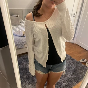 Vit kofta från Bik Bok - Säljer en stilren vit kofta från Bik Bok. Koftan har en rund halsringning och knäppning framtill. Den är ribbad med ett diskret mönster och har långa ärmar. Perfekt för lager-på-lager-stil!