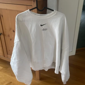 AIK tröja - Säljer en vit sweatshirt från AIK shoppen med aik logga och texten '1891' framtill. På ryggen finns ett stort GNAGET-tryck i svart, vitt och gult. Tröjan har rund hals och långa ärmar. Perfekt för dig som gillar aik. Jag har använt den 3 gånger men jag är inget stort fotbolls fan 
