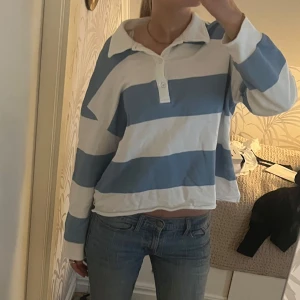 Blåvit randig tröja - En oversized tröja med breda blå och vita ränder. Tröjan har krage, knappar vid halsen och långa ärmar. Perfekt för en dag på stranden eller med ett par jeans till vardags. 