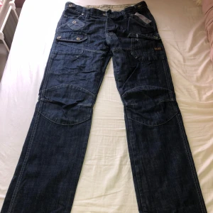 Mörkblå jeansbyxor från G-Star RAW - Säljer ett par jeans från G-Star RAW med flera fickor och snygga detaljer. Saknar en knapp på framsidan (som man ser på bild 2) och en på bakfickan.