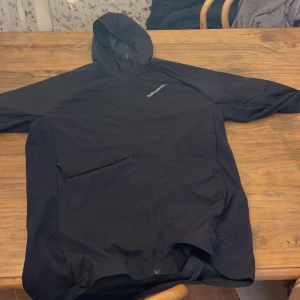 Svart vindjacka från Peak Performance - Säljer en svart vindjacka från Peak Performance med huva och dragkedja framtill. Jackan har diskret logga på bröstet och praktiska fickor. Perfekt för blåsiga dagar och enkel att packa med sig. 