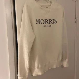 Vit sweatshirt från Morris - Säljer en stilren vit sweatshirt från Morris med svart broderad logga och texten 'EST 1968' på bröstet. 