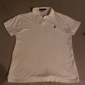Vit pikétröja från Polo Ralph Lauren - Vit pikétröja från Polo Ralph Lauren med klassisk krage och korta ärmar. Slim fit-modell med broderad logga på bröstet. Perfekt för en clean och stilren look.