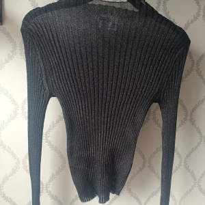 Svart ribbad tröja från Rita Ora x Primark - Säljer en svart ribbad långärmad tröja från Rita Ora x Primark. Tröjan är tight och har en glansig finish som ger en snygg look. Perfekt att styla med jeans eller kjol för en trendig outfit. Lite genomskinlig och därför perfekt som fest topp. Aldrig använd!! Pris kan diskuteras!! 