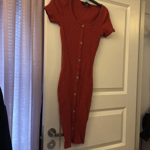 Rostfärgad ribbad klänning med knappar - Säljer en snygg rostfärgad kort  ribbad klänning med korta ärmar och knappar längs hela vägen 