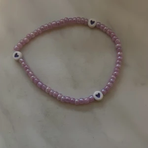 Lila pärlarmband med hjärtan - Sött armband med små lila pärlor och tre vita pärlor med lila hjärtan. Perfekt accessoar för att ge din outfit en gullig touch.